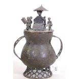 An antique Benin bronze pot and cover, with pierced handles, decorated with a seated chief and