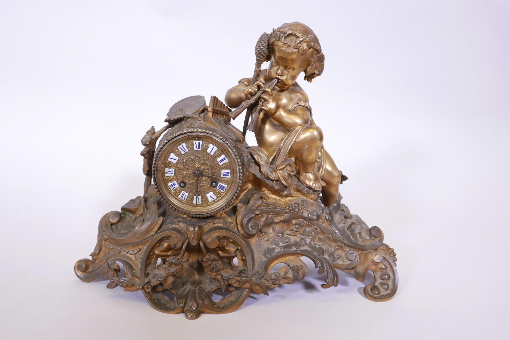 A French brass Rococo style mantel clock surmounted by a putti playing an aulos, with a brass dial