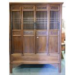 A Chinese fruitwood cupboard with four slatted and panelled doors with carved decoration, raised