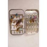 A vintage aluminium fly box containing multiple salmon flies