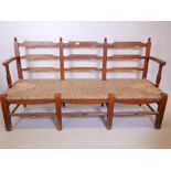 A C19th Continental pine rush seated bench, with shaped ladder back, raised on eight supports united