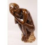 A stoneware figurine of a nude seated upon a rock (signed), 15½" high