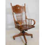 An American ash swivel office armchair with carved back panels, bentwood arms and turned rails on