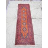 A Persian red ground wool runner decorated with geometric floral medallions, 104" x 34"