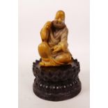A Chinese carved soapstone figure of an ear cleaning master, on an associated carved wood lotus