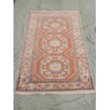 A Turkish Ezine wool rug decorated with three blue and white geometric medallions on a coral