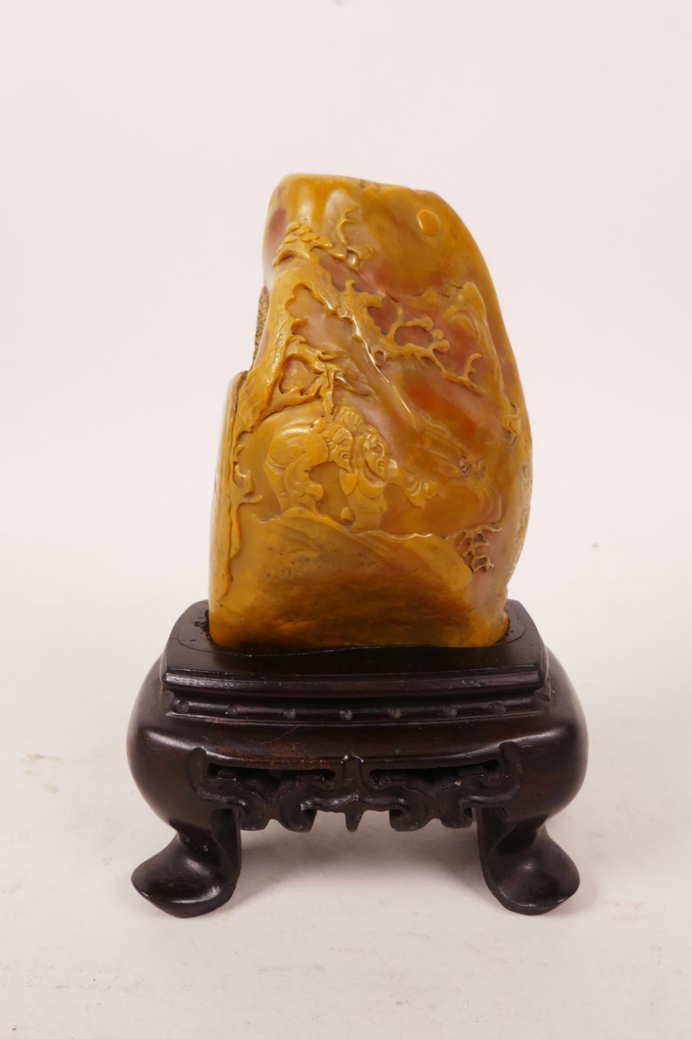 A Chinese soapstone carving of figures in a landscape, on a hardwood stand, 4" high