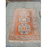 A Turkish Ezine wool rug decorated with three blue and white geometric medallions on a coral