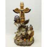 Large model of a Native American kneeling next to a totem pole decorated with wolf heads and an