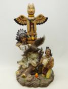 Large model of a Native American kneeling next to a totem pole decorated with wolf heads and an