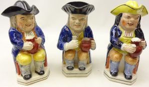 Three 19th century Staffordshire toby jugs all seated holding a jug of ale and a pipe two with hat