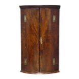 George lll mahogany bow front corner cupboard with moulded cornice above a pair of crossbanded