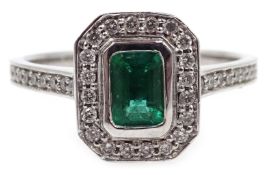 White gold emerald cut emerald and round diamond cluster ring, with diamond set shoulders,