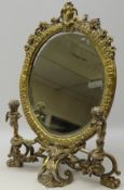 Cast brass toilet mirror with oval bevelled glass panel on open scrolling base,
