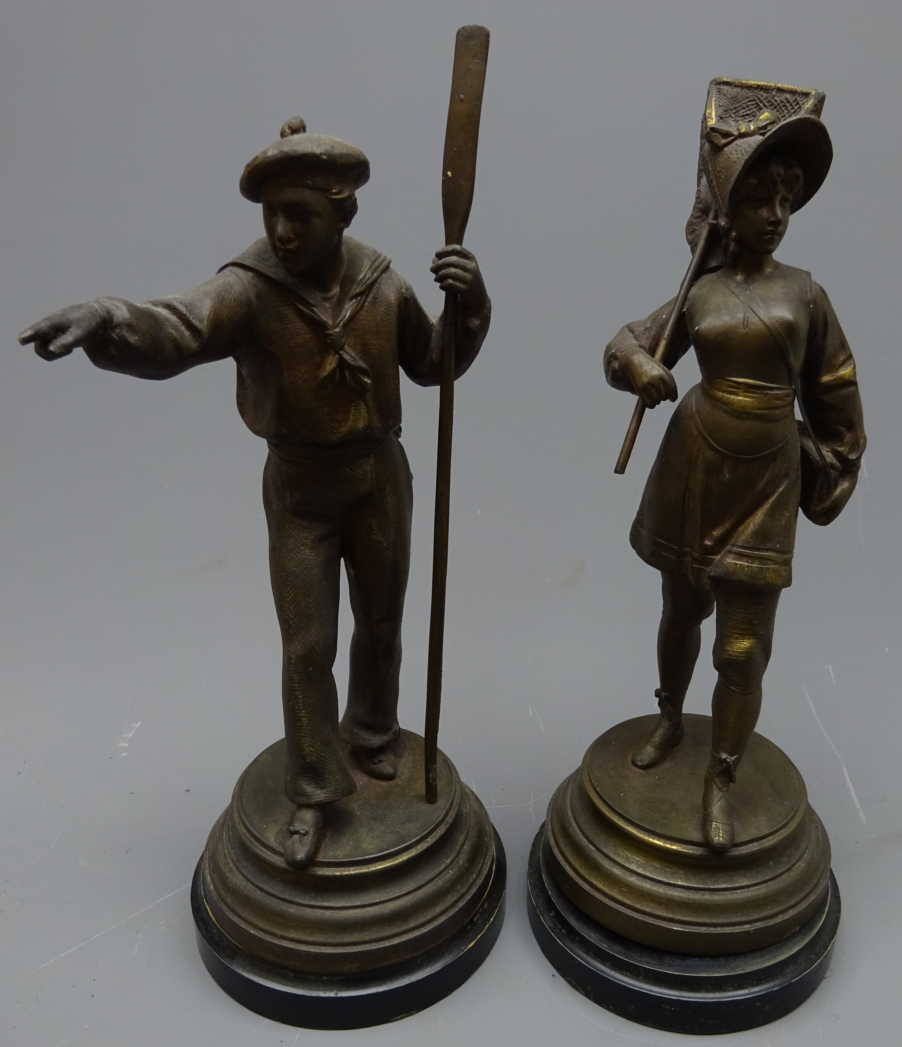 Pair patinated spelter figures of a sailor with oar and fisher girl with net on ebonised circular