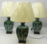 Three Oriental style table lamps decorated with butterflies amongst foliage on turquoise ground on