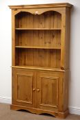Solid pine bookcase on cupboard with two shelves above two doors, on shaped plinth base, W107cm,