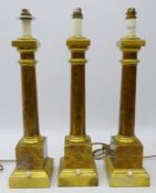 Set of three patinated and polished brass column shaped table lamps on stepped square base,