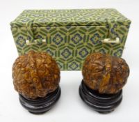 Two Chinese 1000 face carved walnuts on hardwood stand,