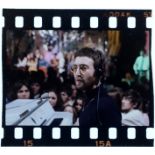 An original 35mm transparency of John Lennon seated in front of a piano at a concert.