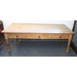 A large pine farmhouse kitchen table, with three frieze drawers on turned tapering legs,