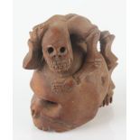 A Japanese carved wood netsuke in the form of a skull, surmounted by a grotesque crawling figure,