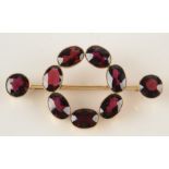 A 15ct gold brooch set with seven oval garnets arranged in a circle upon a bar with a garnet at
