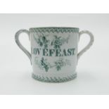 A Victorian pottery loving cup, printed in green with a lakeside palace and inscribed 'Love feast',