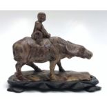 A Chinese soapstone model of a buffalo, with a boy seated on his back, together with a wooden stand,