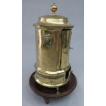 A cylindrical brass plate warmer with mahogany stand, lion mask ring handles, claw feet,