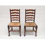 A pair of ash and elm ladderback dining chairs, early 20th century, each with a rush seat.