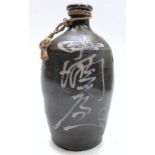 A Japanese stoneware saki bottle, decorated with calligraphy on a brown ground, height 25cm.