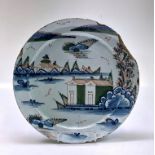 A large English Delft dish, 18th century, polychrome decorated with buildings in a landscape,