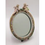 A German porcelain dressing table mirror, surmounted by winged cherubs, height 34cm, width 26cm.