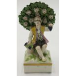 A porcelain figure of a boy, 20th century, modelled holding grapes, seated before a bocage,