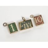 Three gold charms, each contains a folded banknote and each inscribed 'In emergency break glass'.