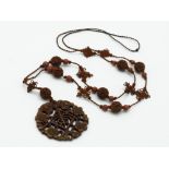 A 19th century Chinese carved wood pendant on a knotted cord necklace with carved beads and