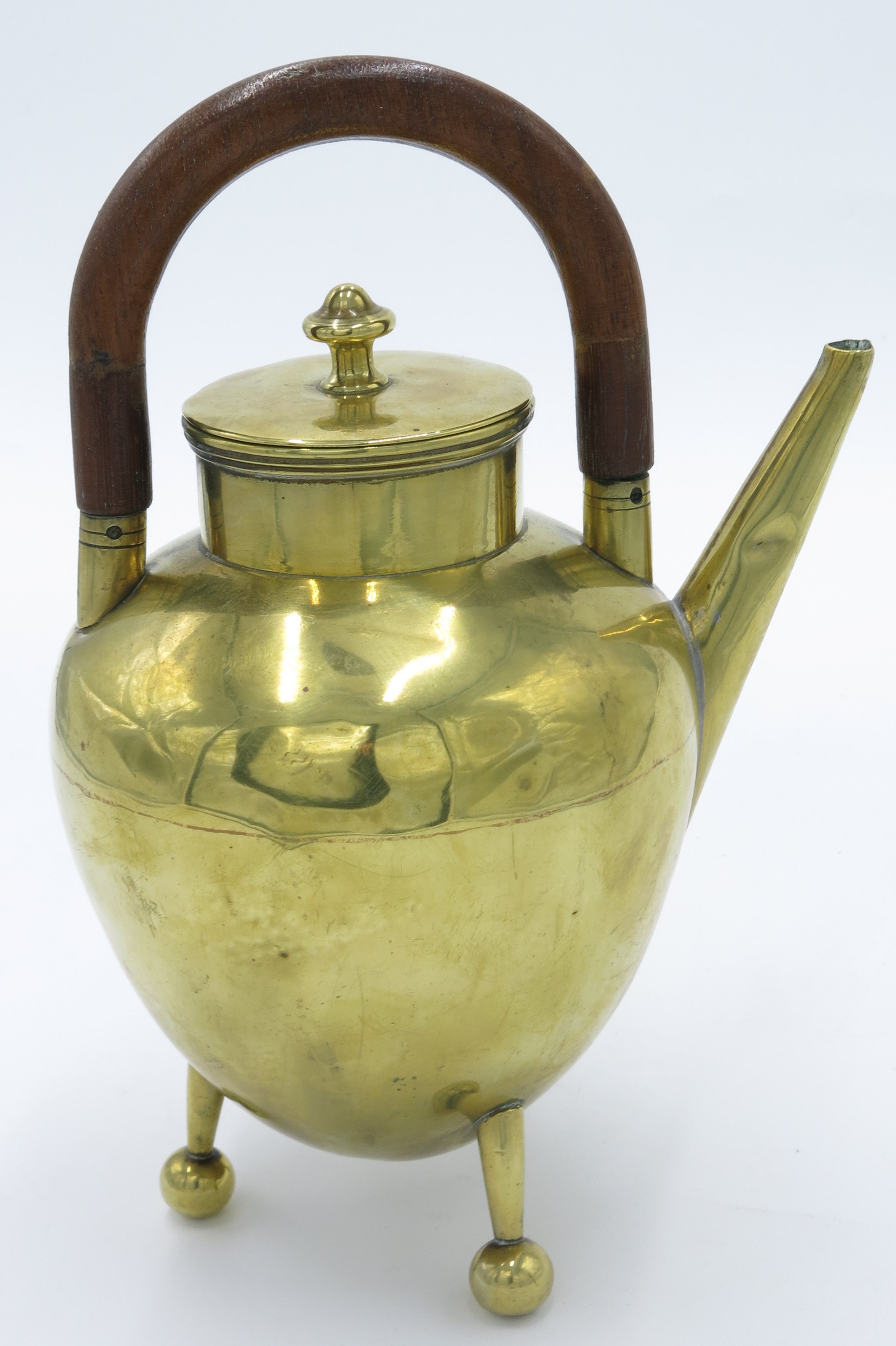 A W A S Benson brass teapot, of ovoid shape with overhead wooden handle and raised upon three legs,