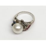 A white gold ring set with a 11.4mm cultured pearl amongst bands of sapphires and rubies.