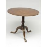 A George III mahogany tripod table, the circular top on a baluster stem and downswept legs,