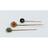 Three gold stickpins each set with diamonds, one with a central tigers eye, the other central coral,