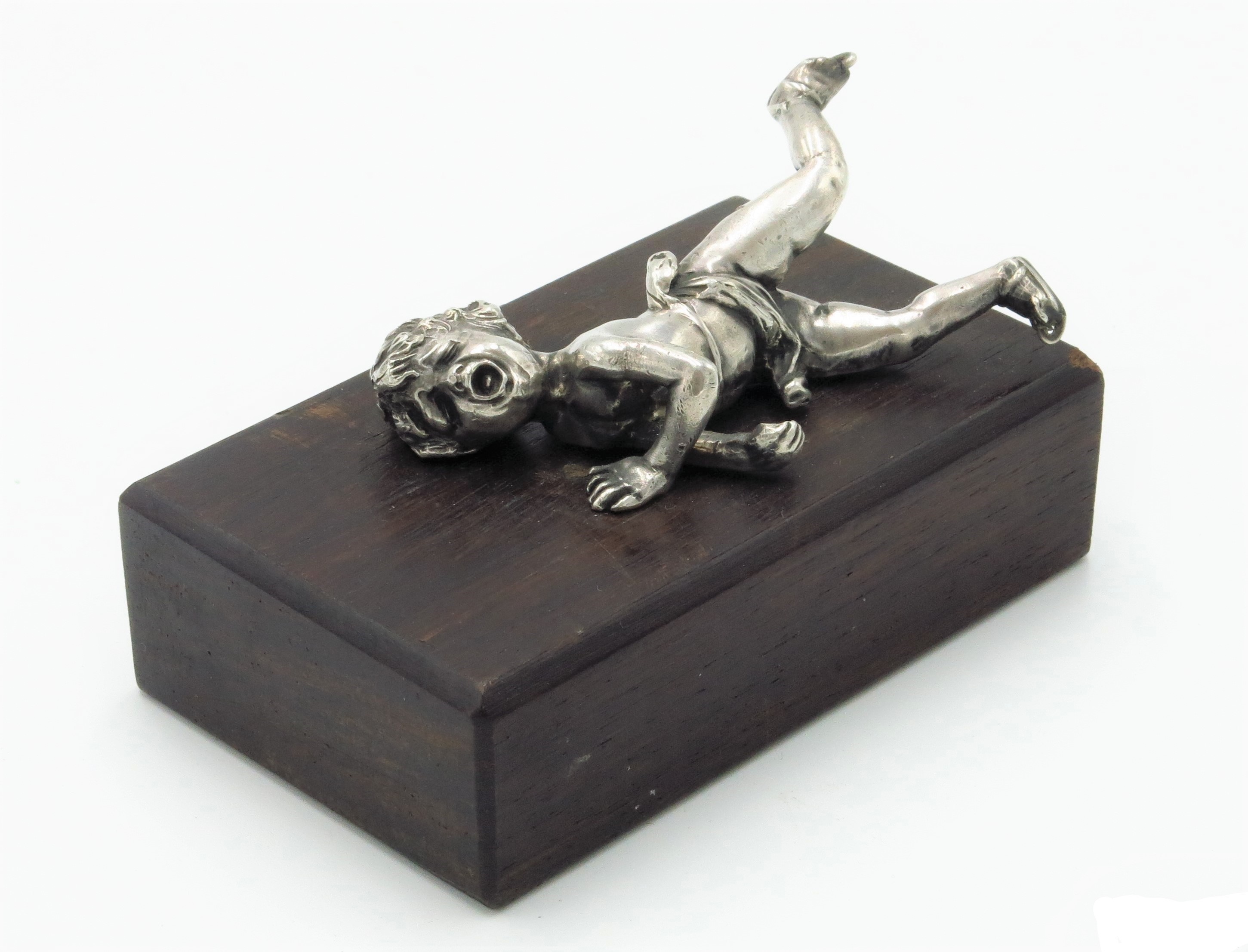 A silver coloured metal figure of a fallen skating putto, on a later wooden stand,