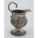 An early George III footed silver cream jug with repousse acanthus decoration and scrolling handle,