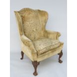 A Queen Anne style wing armchair, with mahogany carved cabriole legs with ball and claw feet,