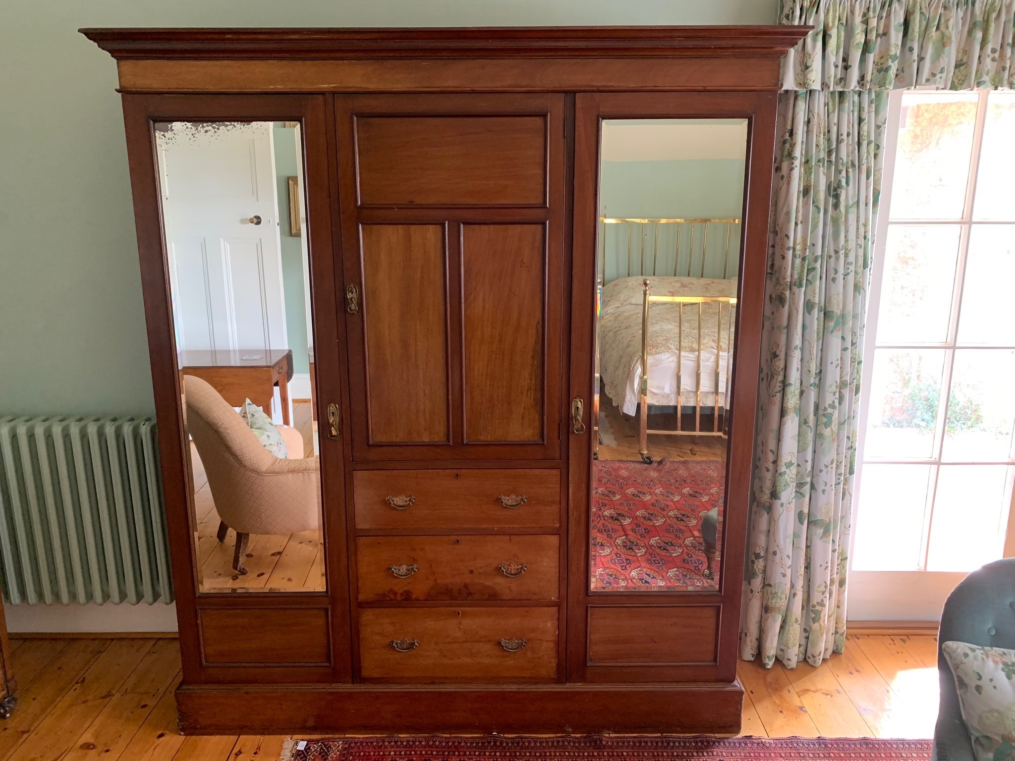 An Edwardian mahogany wardrobe, the central panelled door enclosing fitted shelves, above three