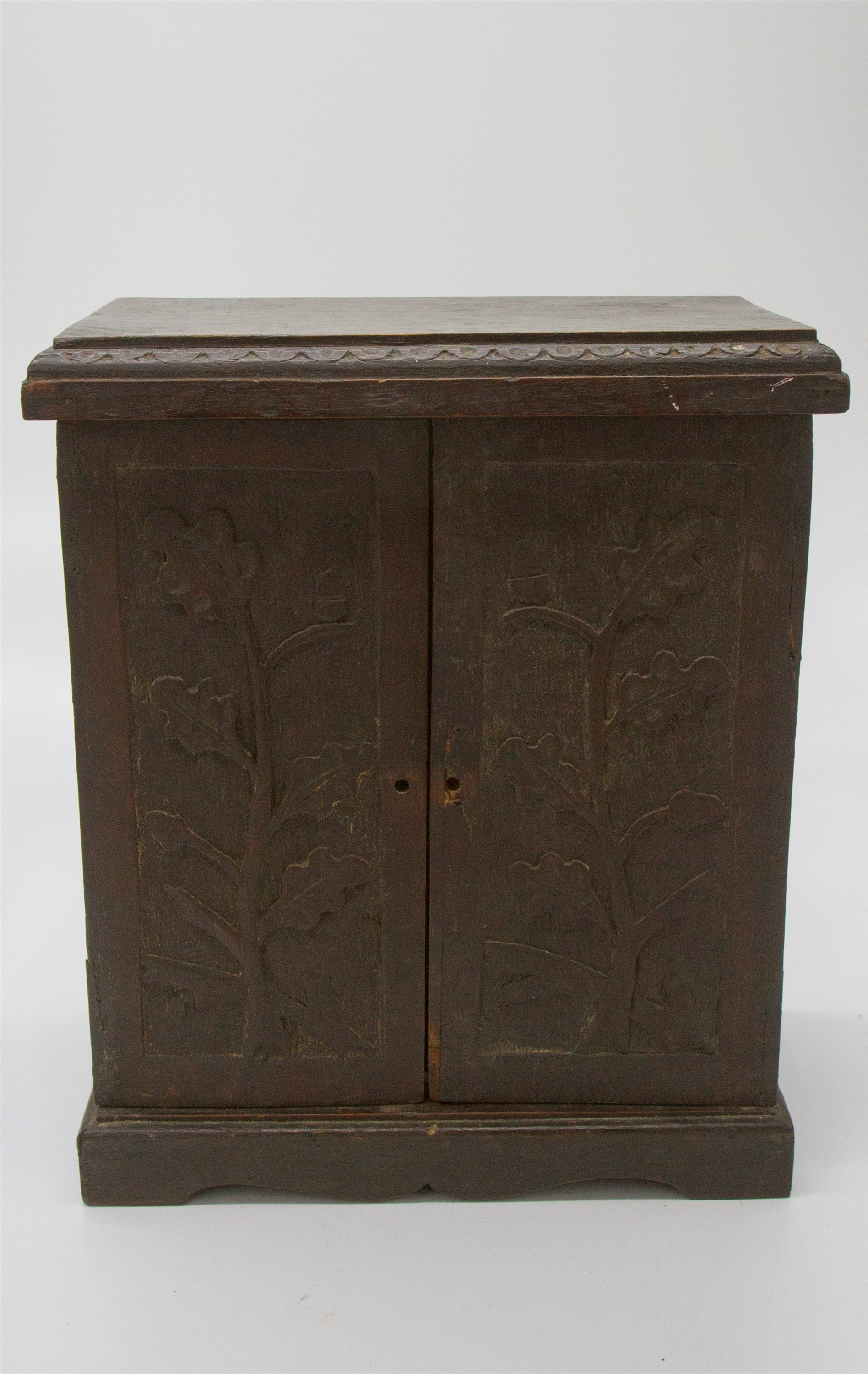 An Arts and Crafts period oak table cabinet, the two doors carved with oak leaves and acorns,