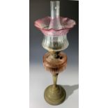 A Victorian oil lamp, with red tinted font, brass column and base and cranberry tinted shade. (