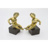 A pair of 19th century gilt brass figures of putti, each seated on a black slate square base. (