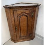 A George III oak corner cupboard, with a mahogany crossbanded arched panelled door opening to reveal