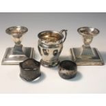 A small silver mug together with a pair of low filled silver candlesticks and two silver napkin
